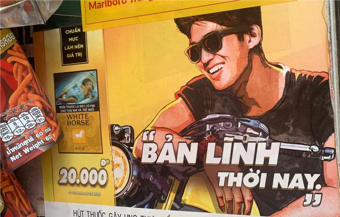 Printed signage advertising cigarettes, featuring a man with sunglasses on a motorcycle, posted at a retailer in Ha Noi